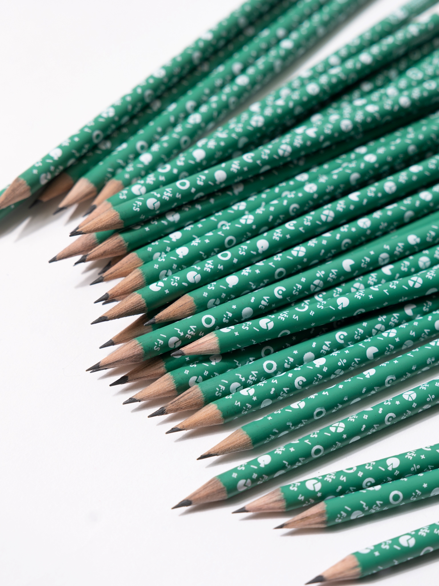 Zelená FIS tužka s malými bílými obrázky grafů, matematických znaků a nápisy F;S. Konec tužky je čistě bílý a nachází se zde guma.