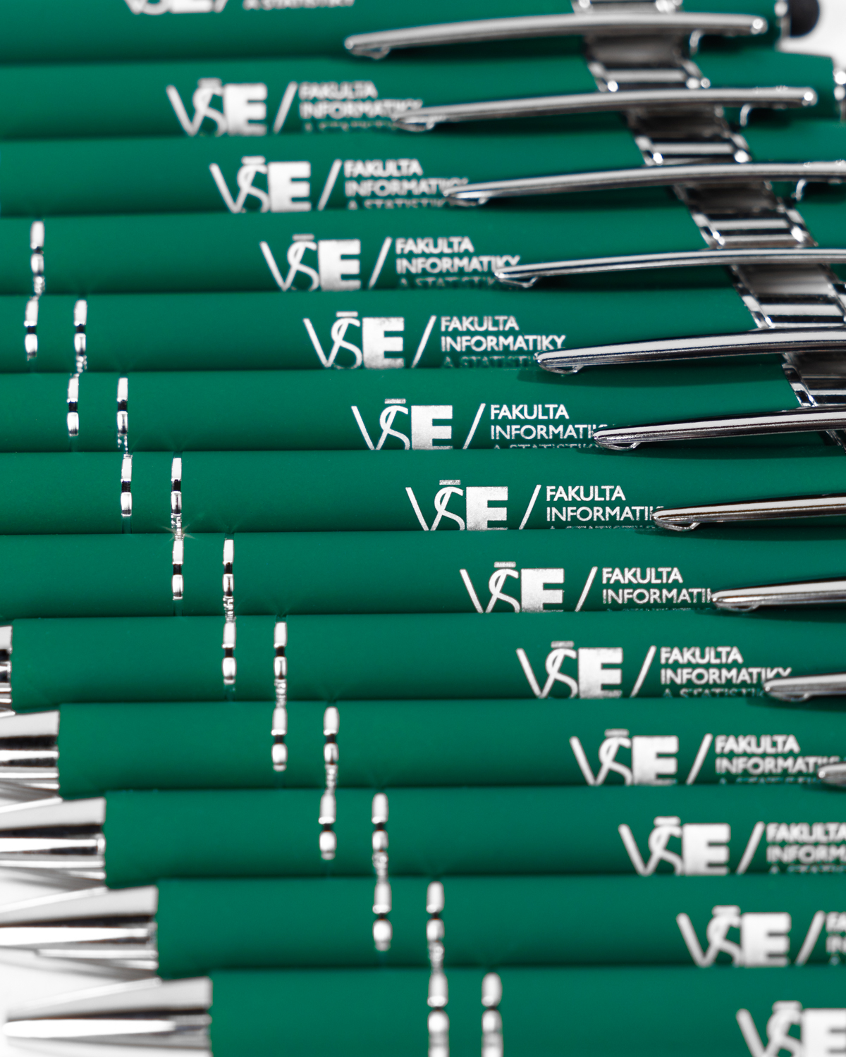 Cvakací zelená FIS propiska se stříbrnými detaily, logem fakulty a černou gumou na konci.