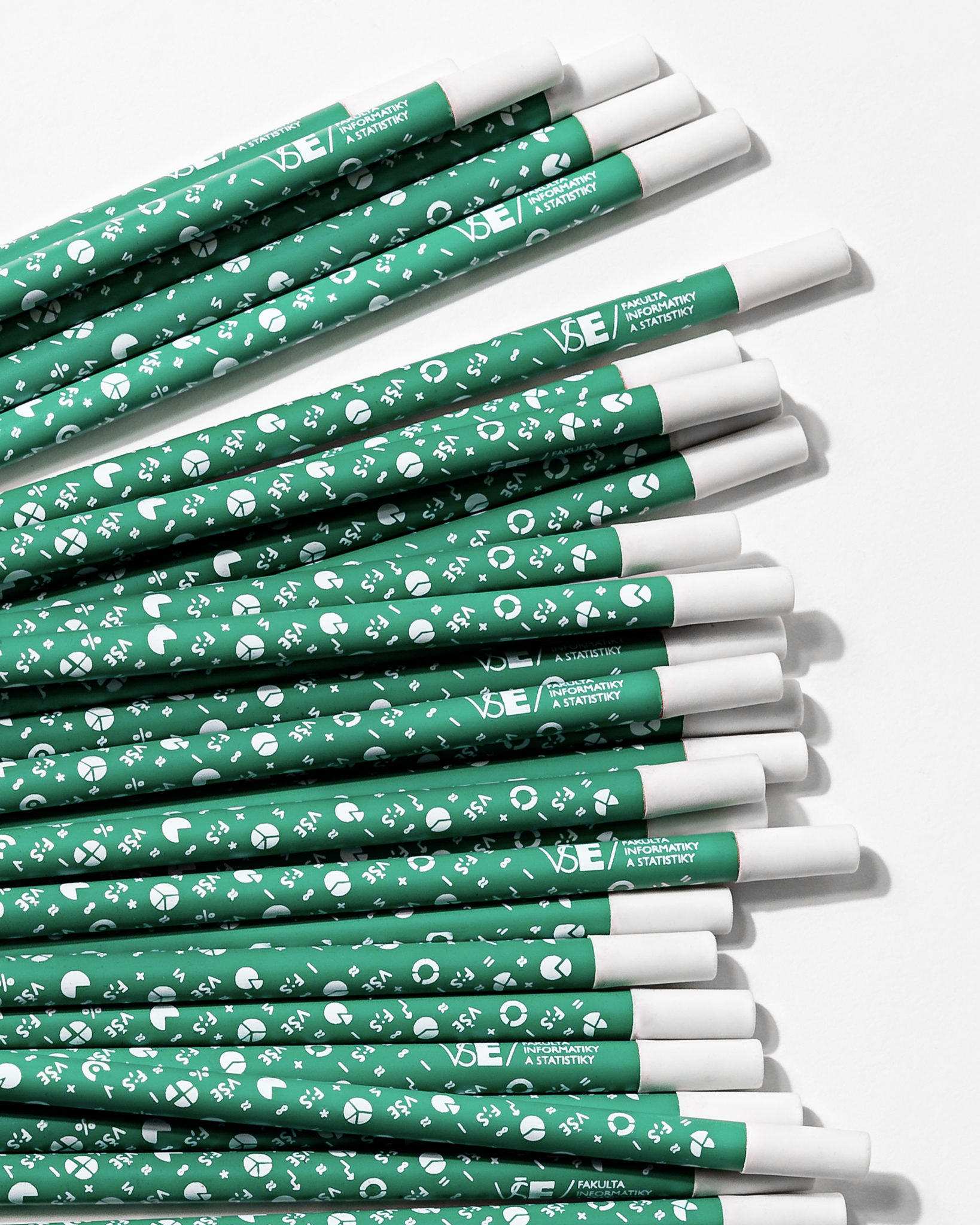 Zelená FIS tužka s malými bílými obrázky grafů, matematických znaků a nápisy F;S. Konec tužky je čistě bílý a nachází se zde guma.